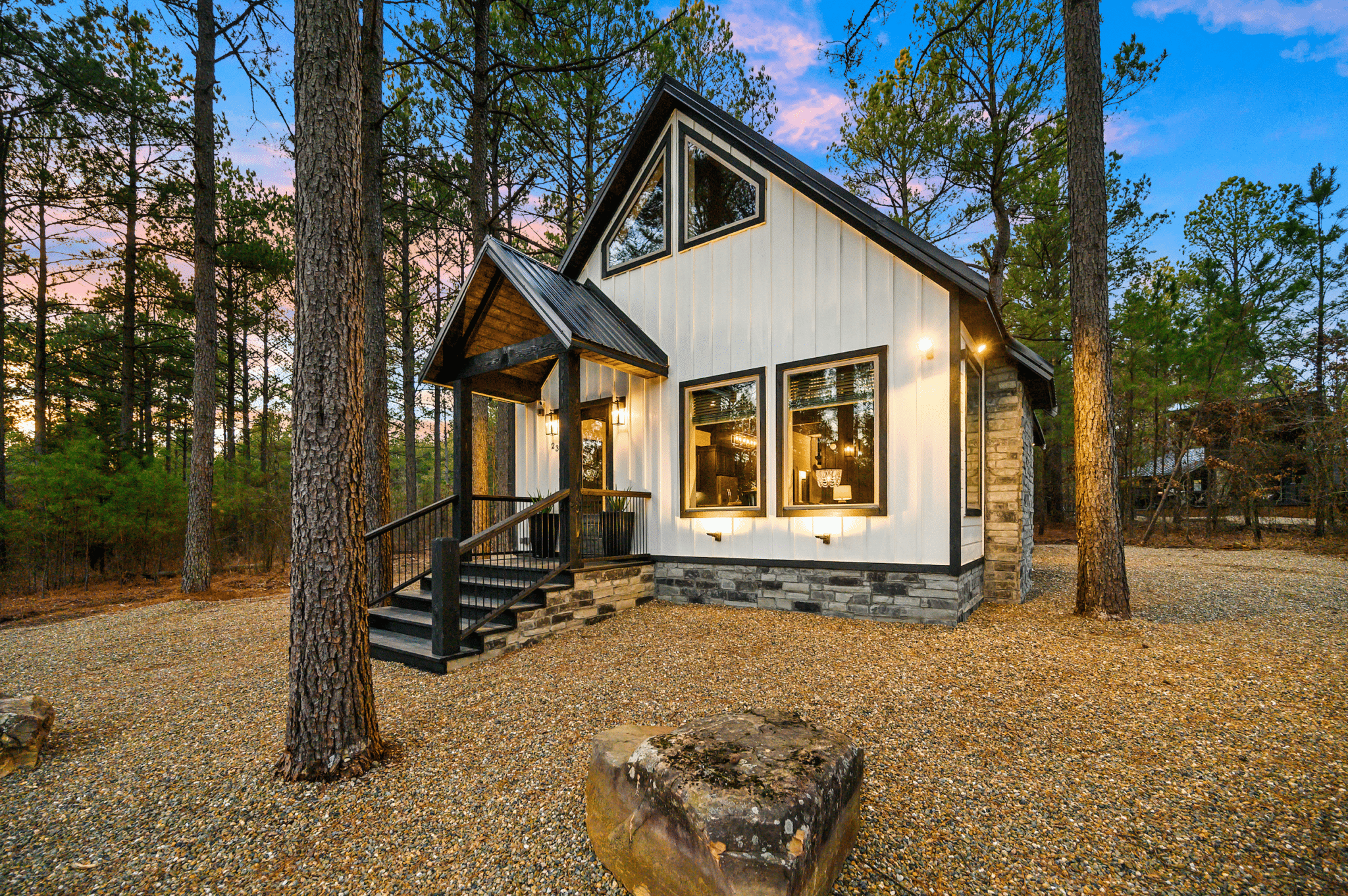 Discover one of our Broken Bow Cabins For Rent Gypsy Tea Room, a white and black cabin set among towering pine trees at sunset.